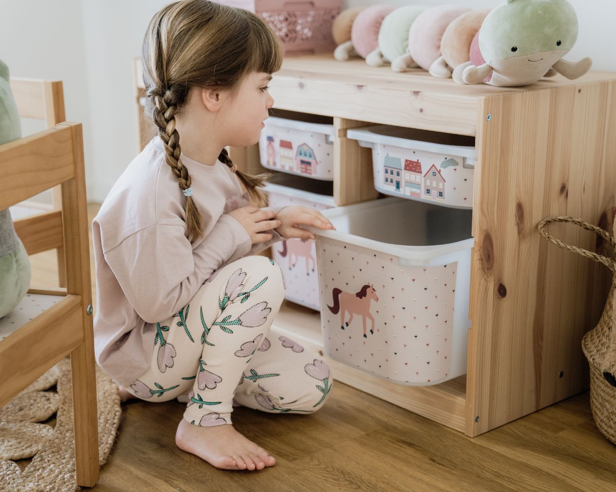 Aufbewahrungsboxen von IKEA mit dem Trofast Regal und passenden Limmaland Klebefolien Ein Mädchen sitzt in ihrem Kinderzimmer und betrachtet ihr Ikea Trofast Regal