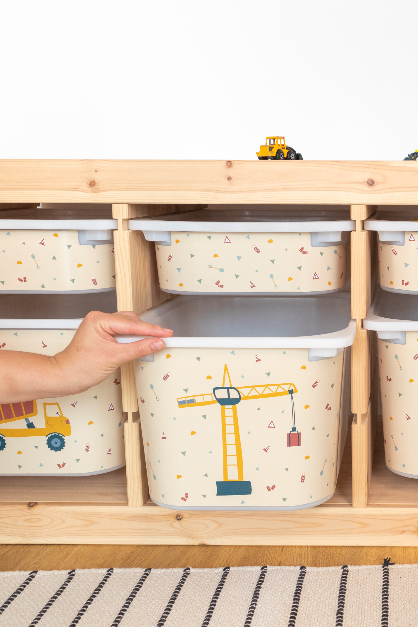 IKEA TROFAST Regal für kindgerechte Baustellen-Aufbewahrung Aufbewahrungslösung im IKEA TROFAST Regal mit einer beige Box, die Bagger, Kran und Kipplader zeigt, passend für das Kinderzimmer.
