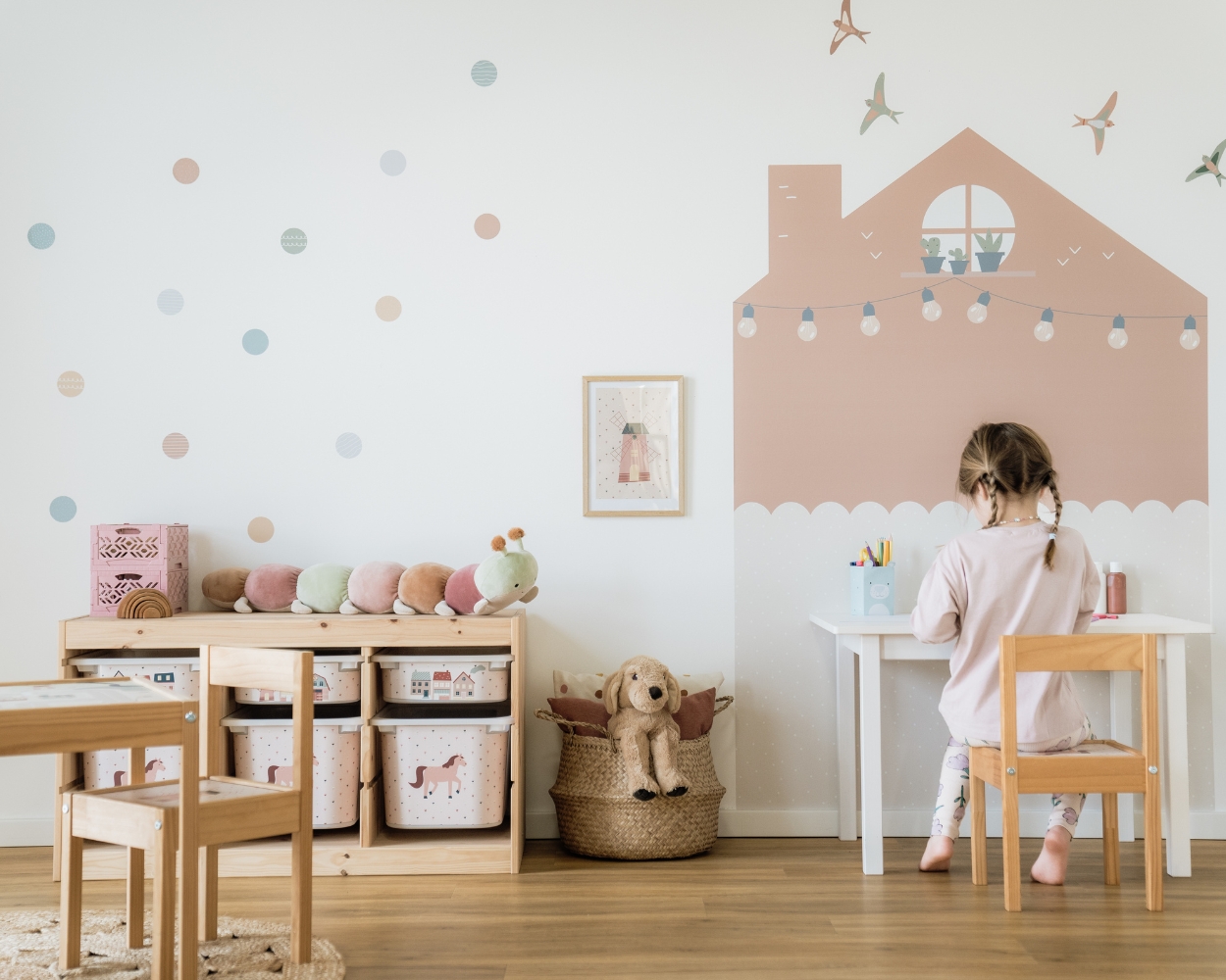 Das Kinderzimmer für Mädchen Ein Kinderzimmer für Mädchen mit rosa Wandtattoos, einem Ikea Trofast Regal mit Klebefolien mit Pferden, ein Tisch und ein Mädchen, welches an ihrem Schreibtisch stzt